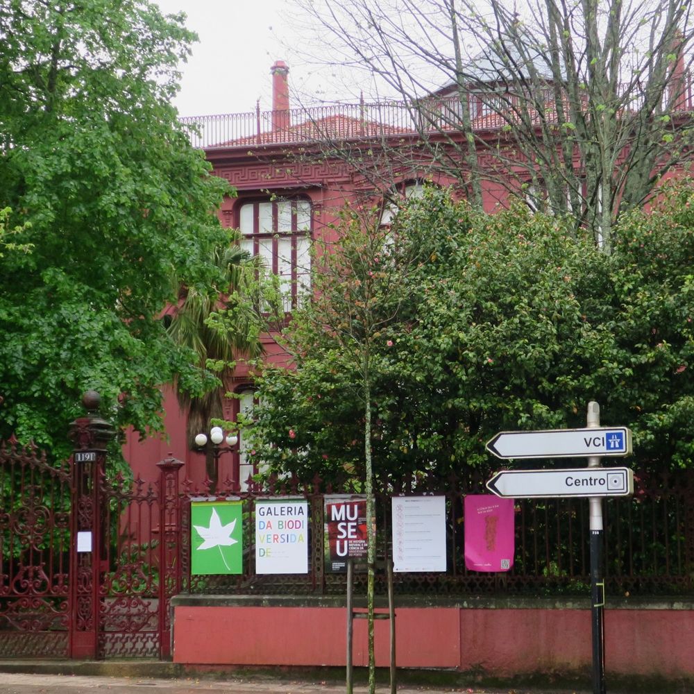 A magenta buiding within a garden with tall trees - Hall of Bioversity of the University of Porto..