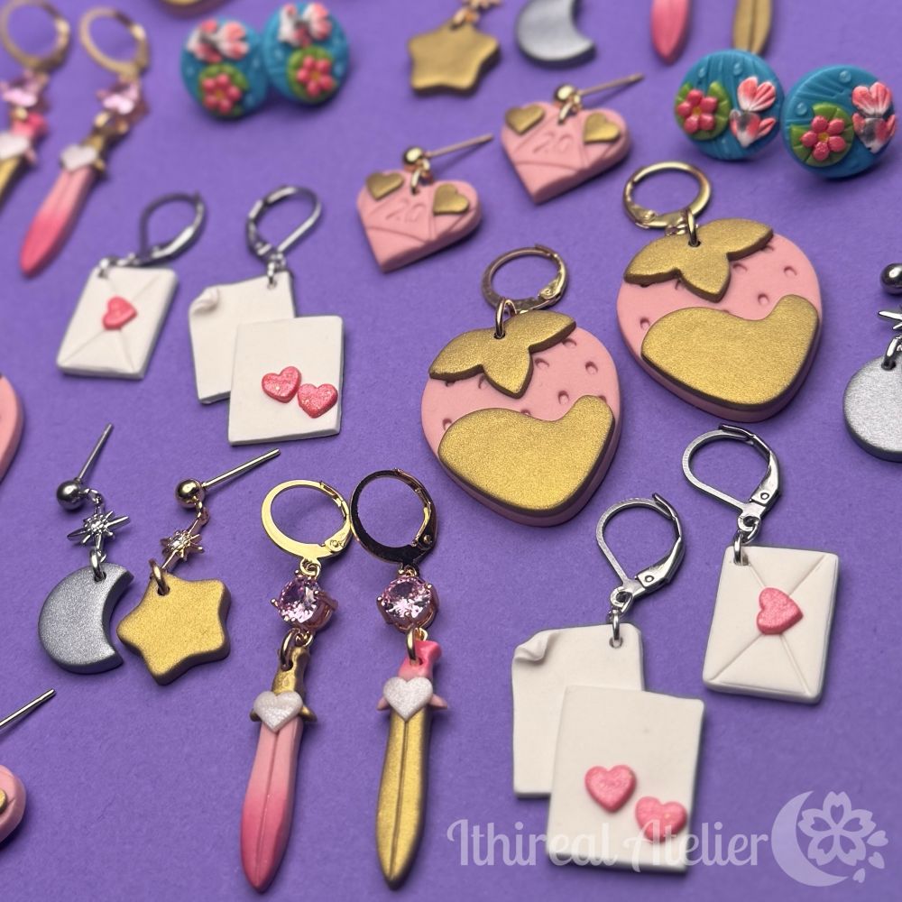 Many different styles of handmade polymer clay earrings on a purple background. They are love and Valentine’s themed, with pink being the most used colour. 
