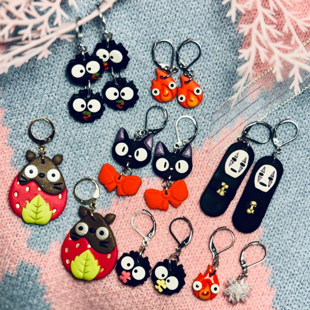 Seven pairs of different Ghibli-themed polymer clay earrings laying flat on a Howl-coloured fabric. 