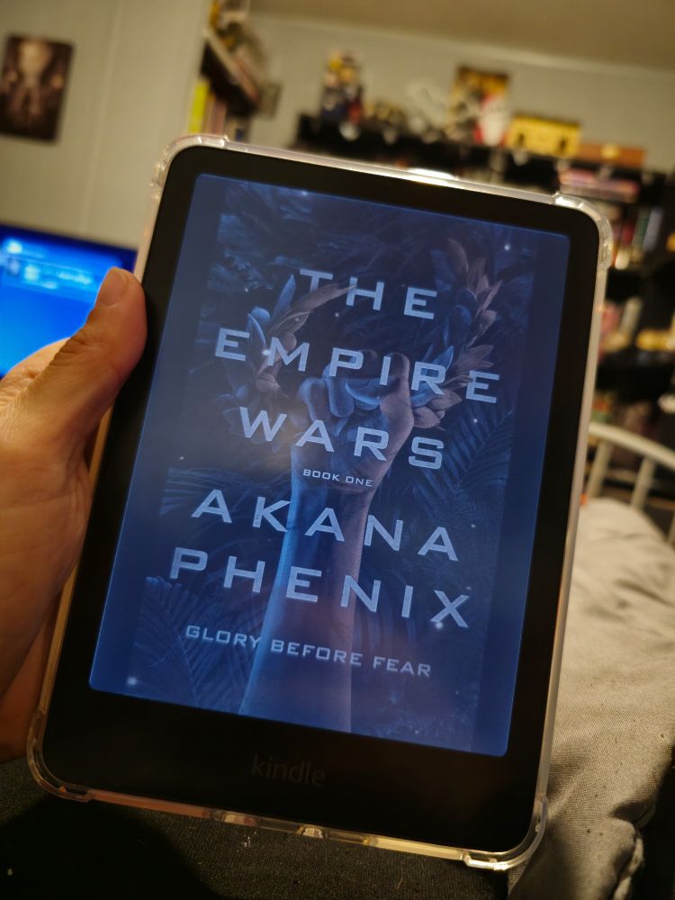 My hand holding a kindle colorsoft displaying the cover of The Empire Wars by Akana Phenix 