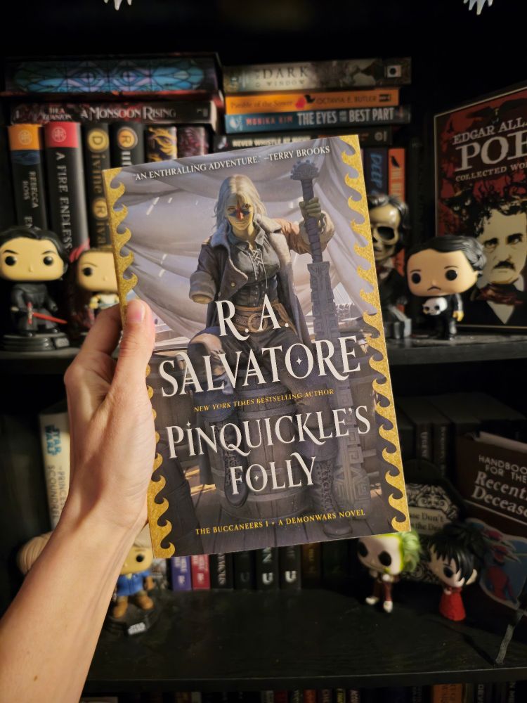 My hand holding a paperback copy of Pinquickle's Folly by R.A. Salvatore 