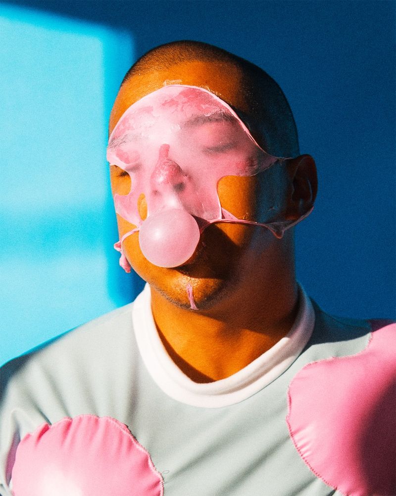head shout self portrait blowing a bubble with bubblegum. a previous is bubble is popped all over my face. gum is  bright pink against a blue backdrop.