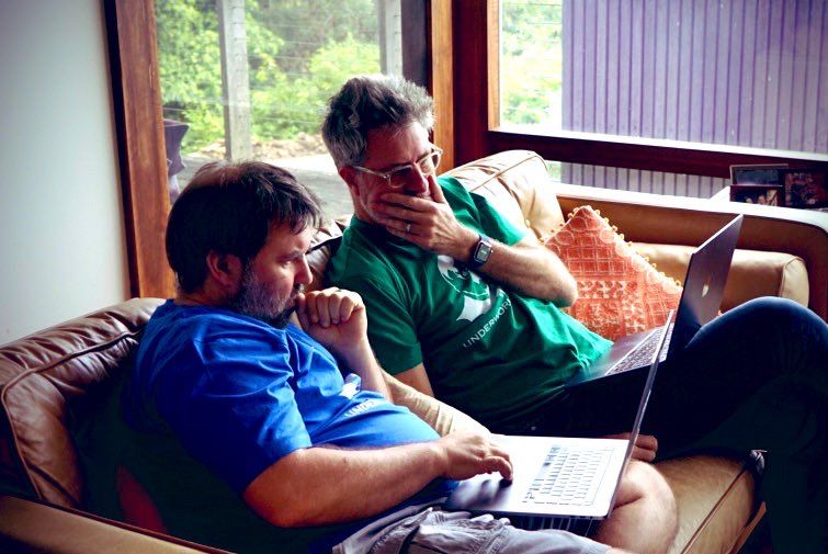 Thing one and thing two sitting on a sofa working on laptops. Classic human pretending to ponder deeply poses (scratching chin / biting nails)