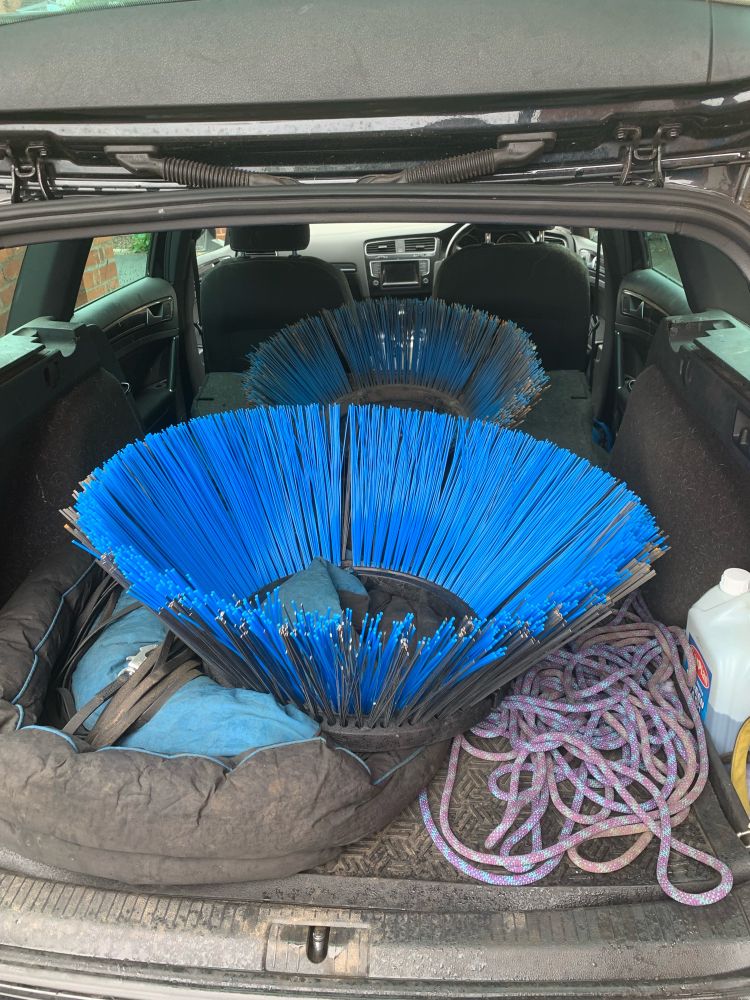 The back of an estate car, containing two brush heads taken from street sweeper machines. One is brand new, one is used. The steel bristles are to be recycled to make lock picking tools. 