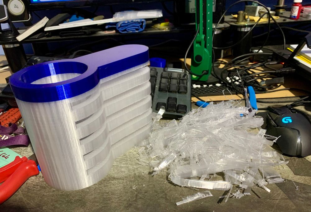An oversized 3D printed cutaway lock part, next to a pile of bridging material I’d just removed on a messy desk. 