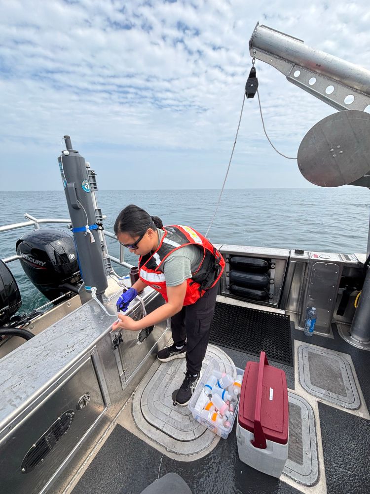 A researcher collecting water samples from a Niskin bottle on a boat on Lake Erie.