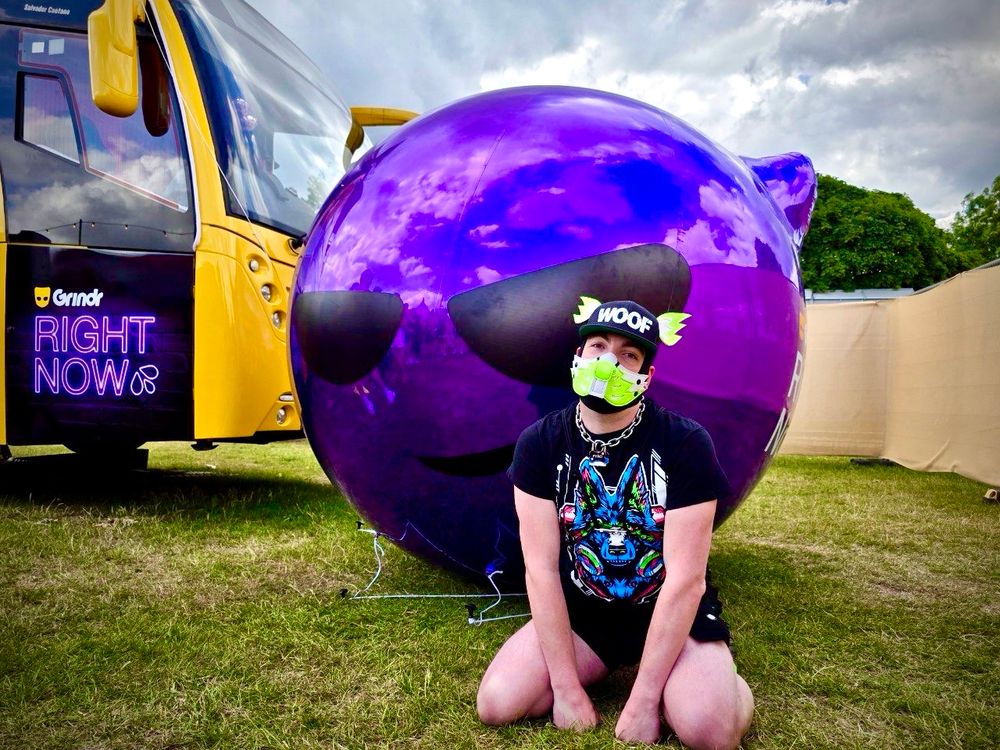 A human pup sits like a good boy in front of the devil emoji and the Grindr tour bus