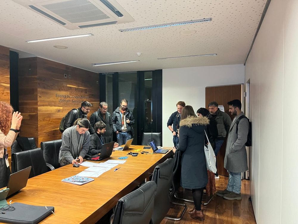 A group of 10 people are grouped around a table and they are looking at three players enjoying Minecraft on their laptops. They all seem to be very focused on the game