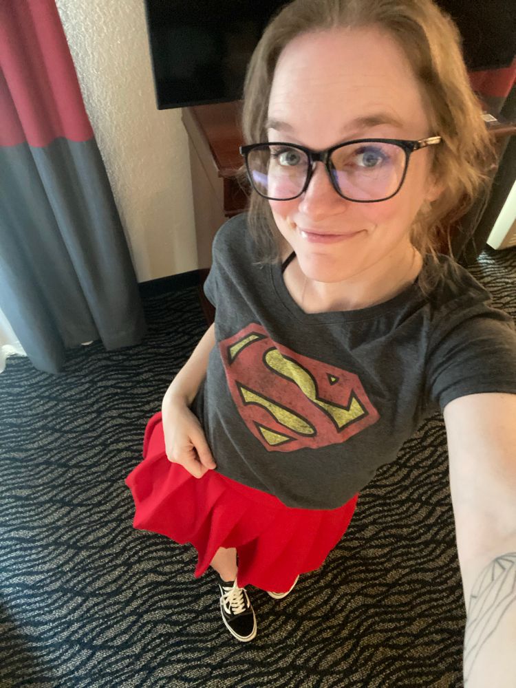 Megan wearing a Superman tshirt & red skirt & black “Clark Kent” glasses & black vans