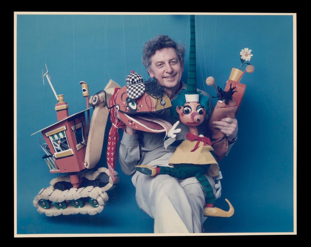 A man sits surrounded by marionettes