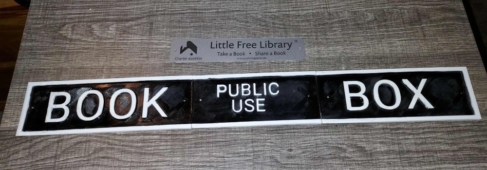 A metal little free library sign over a parody of the Police Box sign from the TARDIS saying Book Box