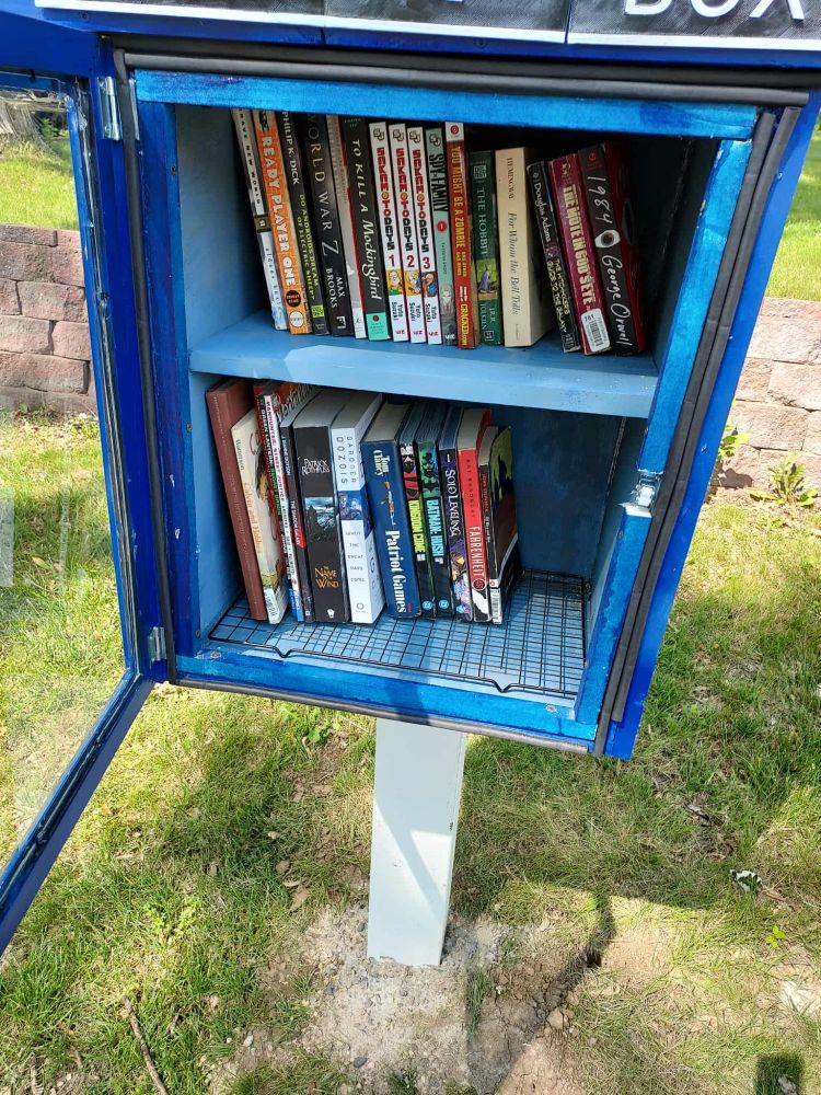 A little free library with the door open to show a tray inside and the weather stripping around the door.