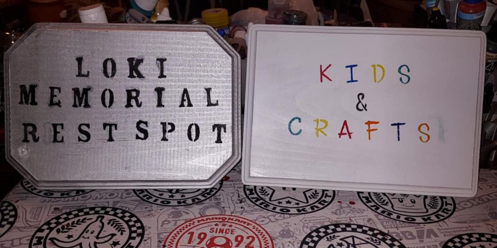 Used stencils for the letters on two signs, one, a wood plaque painted silver with black letters saying 'Loki Memorial Rest Spot' and a white plaque saying 'Kids & Crafts'