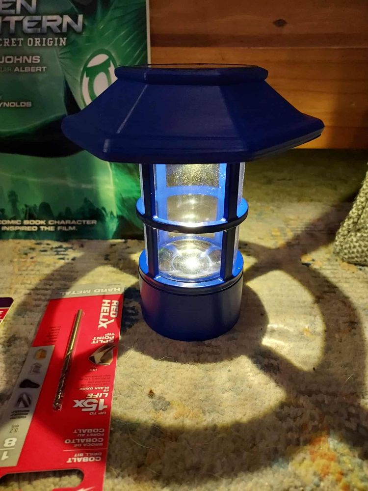 The lantern for the top of my themed Little Free Library with a printed shade on it. It's lit and casting a shadow around it, and it's all painted blue.