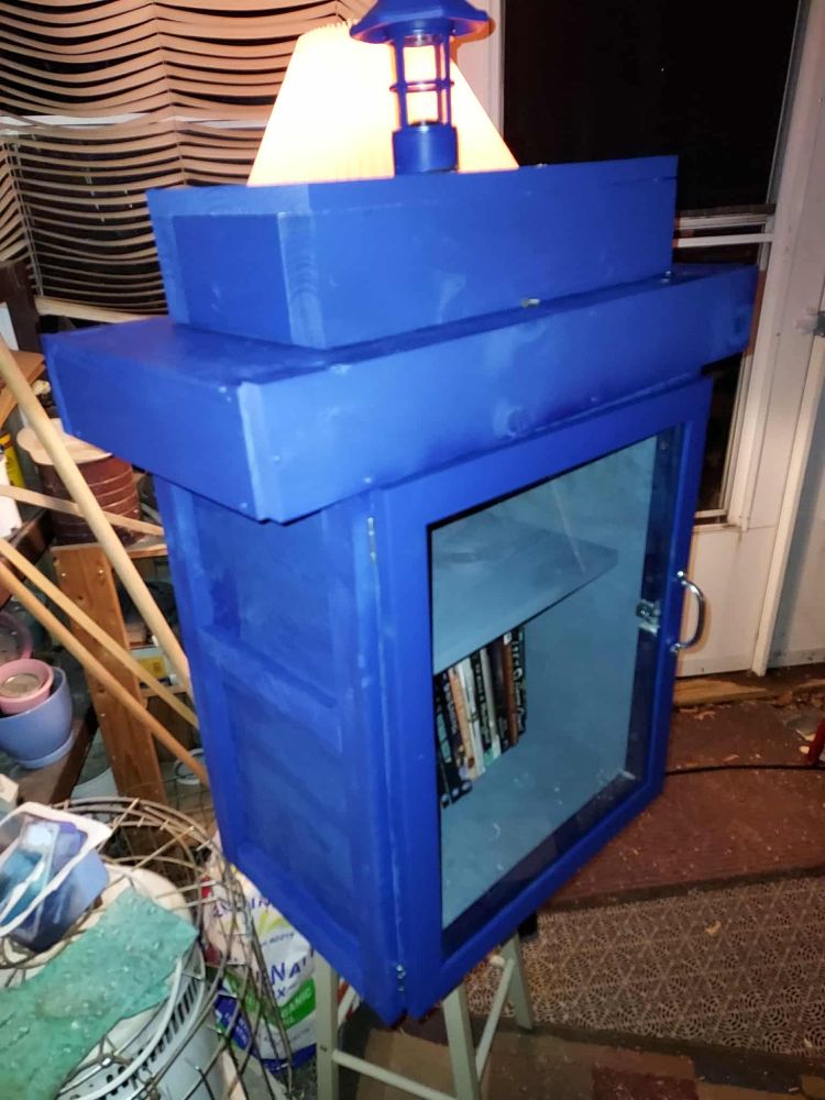 A blue little free library box, designed like a TARDIS from Doctor Who, sitting on a stool with a door installed.
