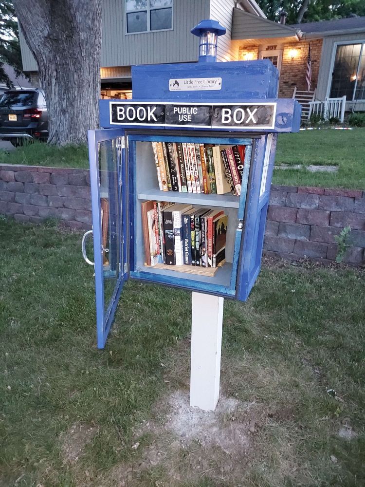 The little free library loaded up with books, its door opened and showing its latch.