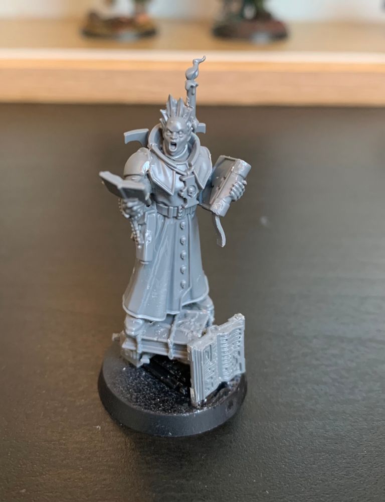 An unpainted mystic operative miniature, standing on a pyre made of books.