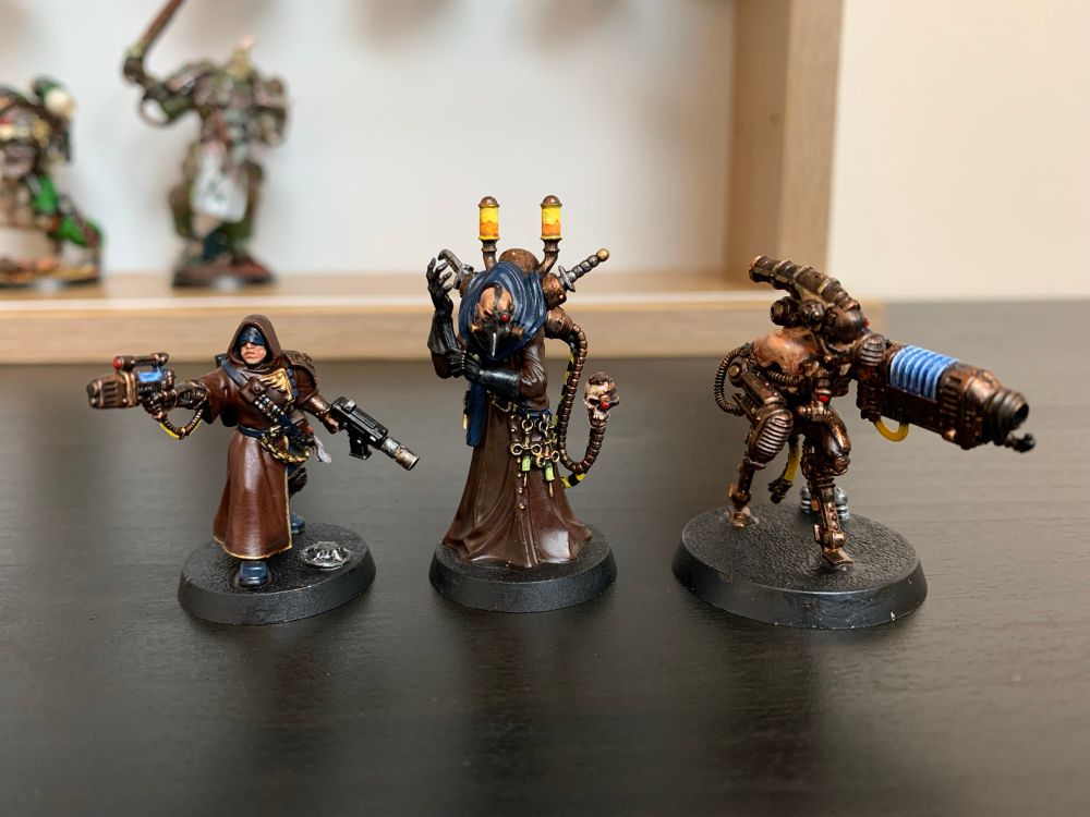 Three painted miniatures from an Inquisition kill team - a Pistolier operative, an Enlightener (based on Doctor Arachnos from Necromunda) and a converted gun servitor.