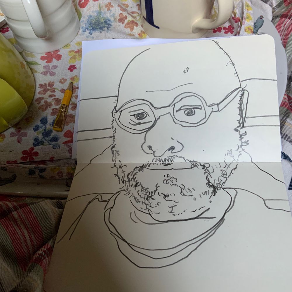 A sketchbook in portrait orientation sits over the corner of a tea tray covered in a floral cloth. To the left of the sketchbook sits a yellow pencil stub with a blunt lead and a gold ferrule with the remains of a yellow eraser peaking out of  its end. The pencil stub is shorter than the ferrule. Also on the tray and surrounding the sketchbook the handles and bases of, a green teapot, a milk jug and cream-coloured mug are just visible. The mug has what looks like a capital "M" on its side. An illustration of a grey chicken is visible on the top right of the try handle.

In the sketchbook is a self-portrait spreading across the two visible pages. It is made with bold, thick pencil lines  and is of a bearded bald man in his fifties sitting up in bed. He is wearing round glasses and a t-shirt and has heavy lines under one of his eyes, suggesting that he might be a little weary.
