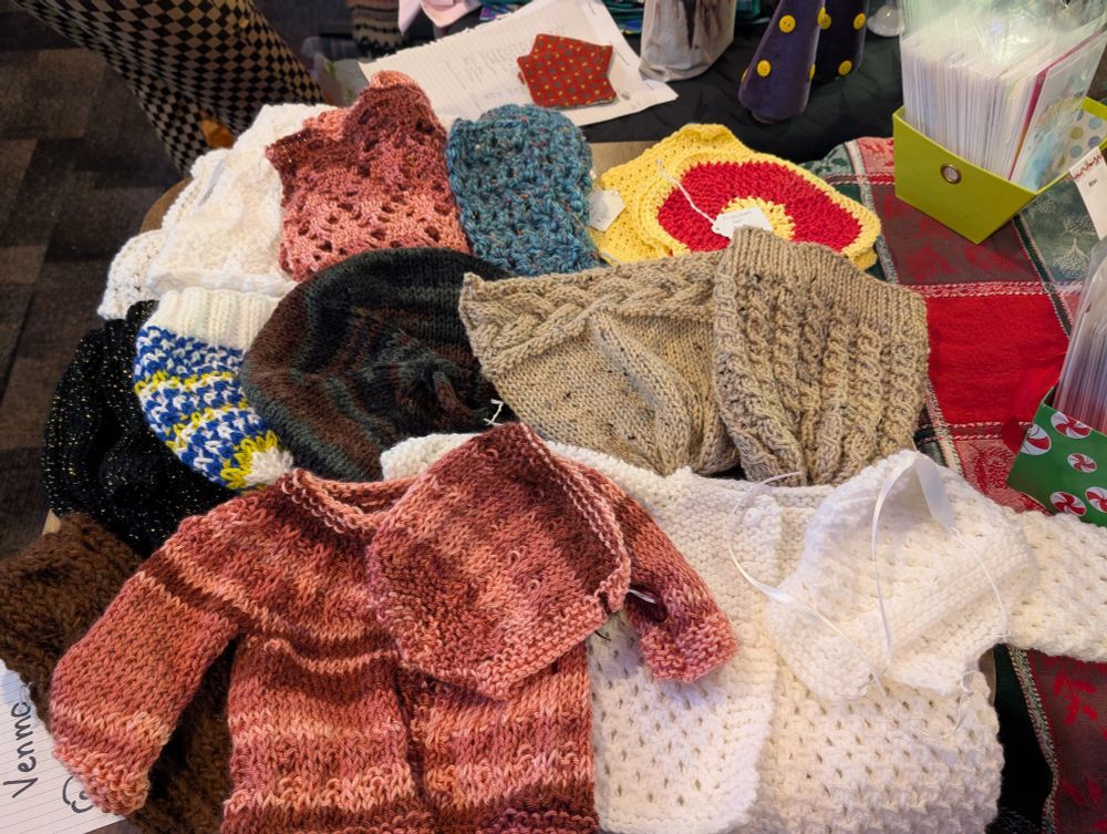 My table at the Spot with two baby sweaters, a bunch of knit hat, crochet scarves, and dish clothes. 