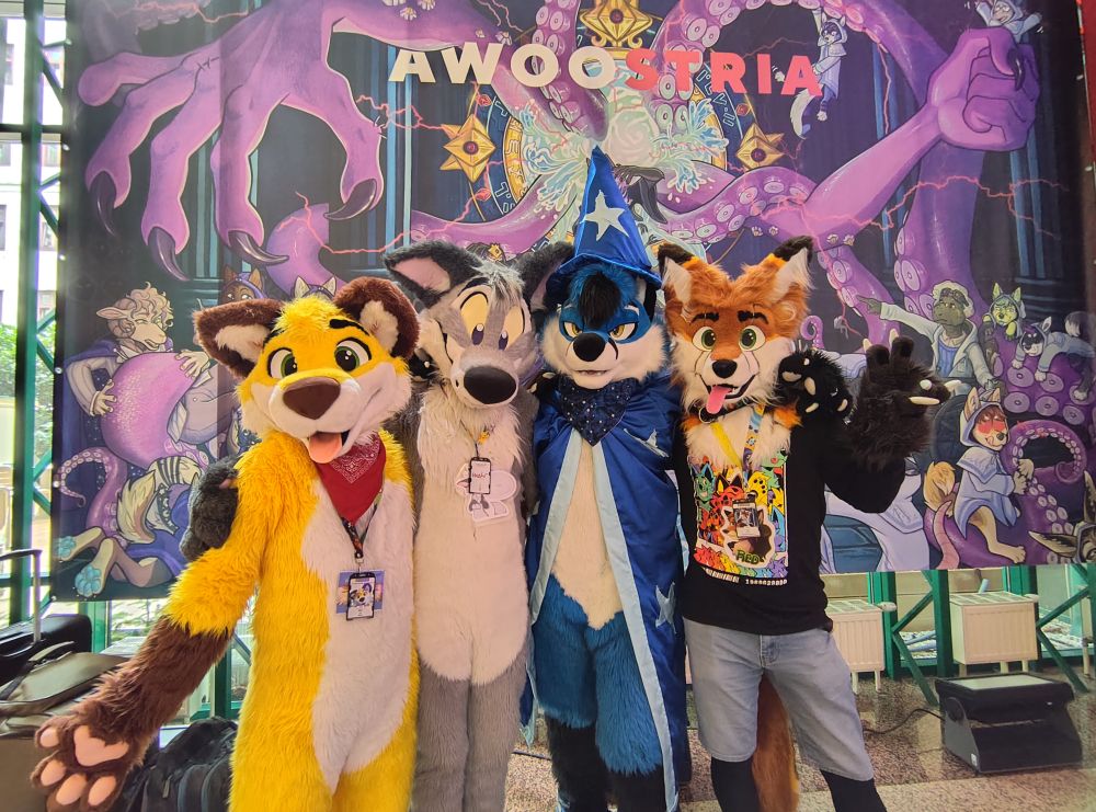 Four foxes (Nico, Tabbie, Blujay, Red) posing by the Awoostria themed art decoration in the lobby. Photo by @sharkythewhite.bsky.social