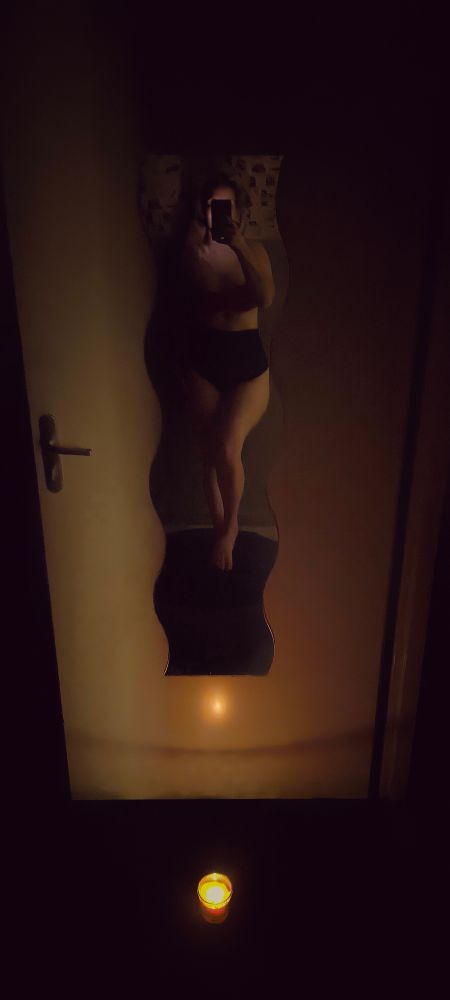 Lady Peri en culotte noir, face à un miroir avec une bougie au sol