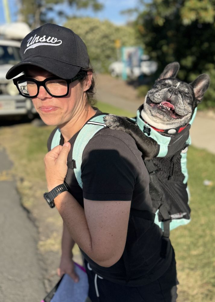 Person in a hat carrying a French Bulldog in a backpack.
