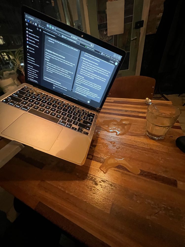 Holding laptop in my left hand, because the coffee is dripping from it on the small wooden table where is the rest of the coffee. You can see that it’s dark outside through the window that is behind the laptop. On table is a spilled cup of coffee, metallic spoon and headphones making this composition of a complete mess