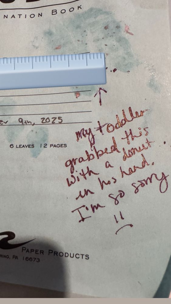 Blue book exam with splotches of strawberry donut on it that says “my toddler grabbed this with a donut in his hand. I’m so sorry.” In my handwriting 