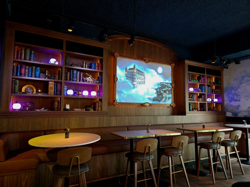 A large bookshelf with trinkets on the shelves and a large painting in the centre behind some tables, sofas, and chairs.