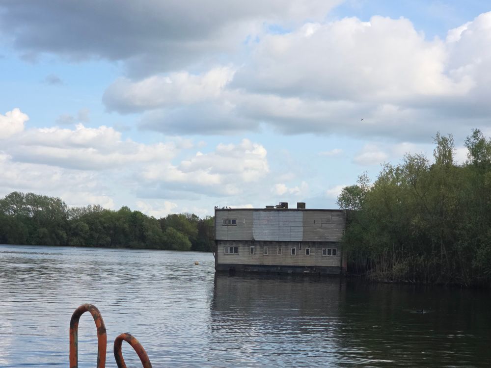 A photo of an abandoned grey building from across a large body of water.