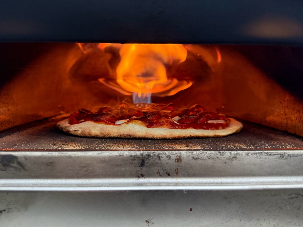 A pizza cooking in a small oven, topped with pepperoni and cheese. Intense flames rise from the rear, creating a comforting glow.