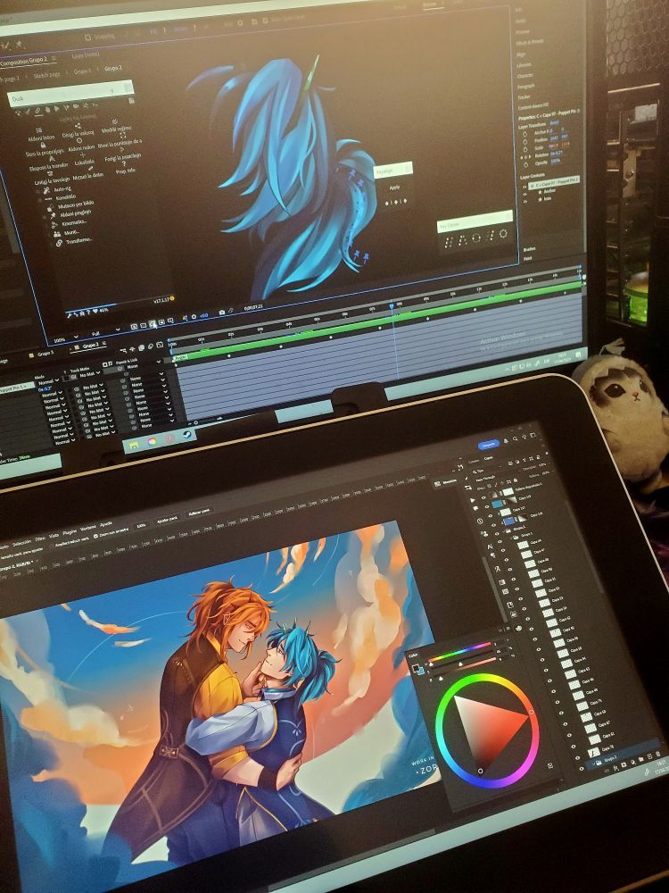 A photo showing a dual-screen digital art setup. On the top screen, After Effects is open, displaying an animation project focused on flowing blue hair with multiple layers on the timeline. On the bottom screen, a tablet shows a vibrant illustration in Photoshop of two male characters in a romantic embrace under a dreamy sky with warm, fluffy clouds. One has long red-orange hair, the other blue hair; they gaze into each other's eyes lovingly. A color wheel is visible on the screen. A small plushie is tucked beside the tablet.


