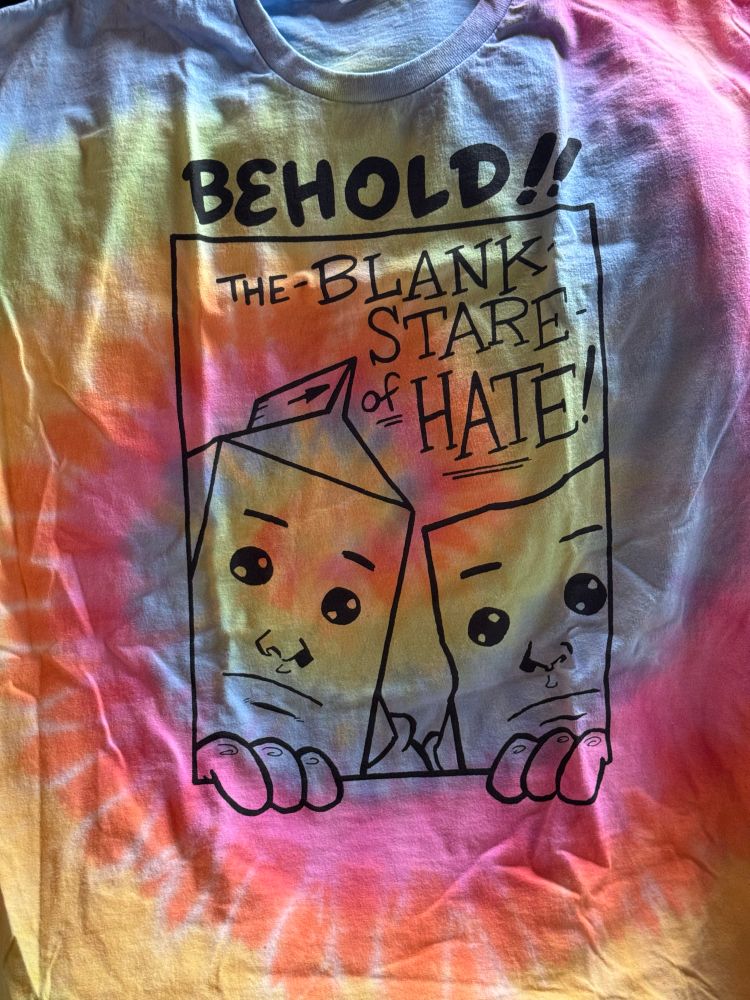 A cartoon milk carton & a wedge of Swiss cheese look blankly through a rectangular portal at the viewer. Accompanying text reads: “BEHOLD!! The BLANK STARE of HATE!”