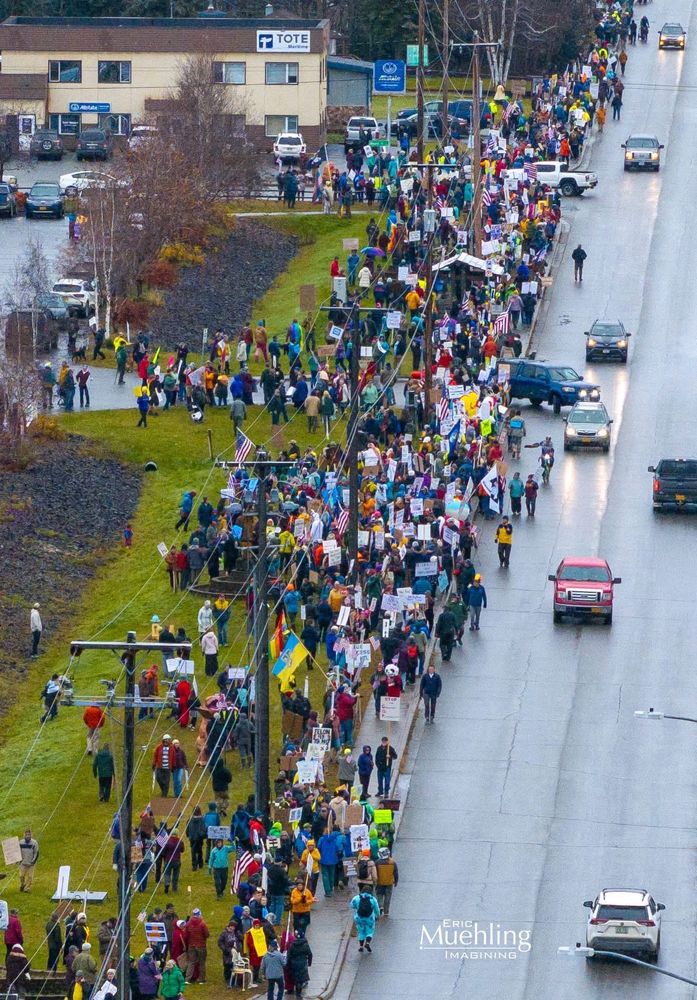 A crowd of people standing along the side of the road in front of Pioneer Park in Fairbanks, Alaska, for the No Kings protest on October 18, 2025