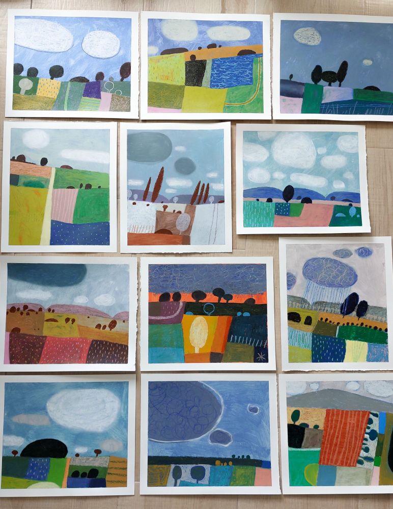 A photo of twelve colorful abstract landscape paintings laid out on the floor 