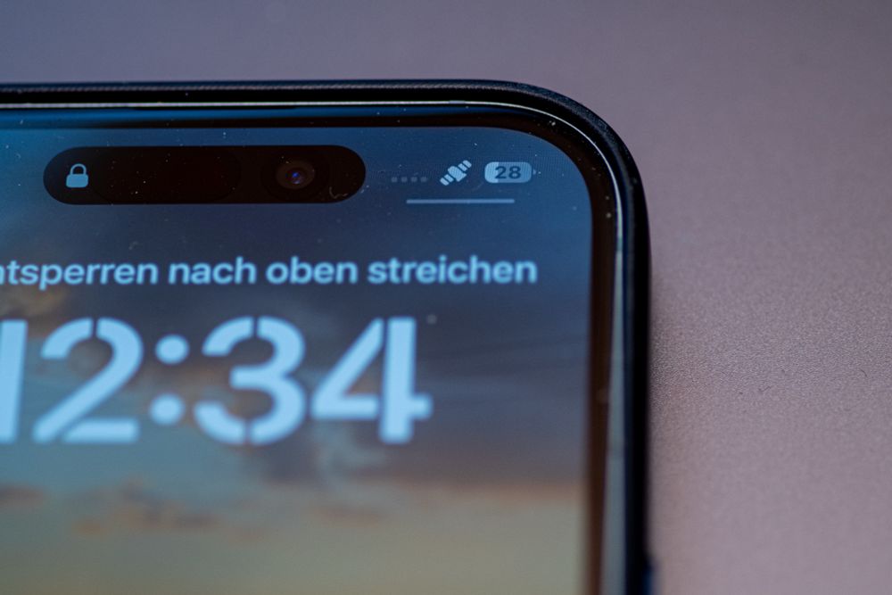 Die obere rechte Ecke eines Smartphones, man sieht die Uhrzeit und darüber einen Text, ganz oben wird eine stilisierter Satellit und der Füllstand der Batterie angezeigt.