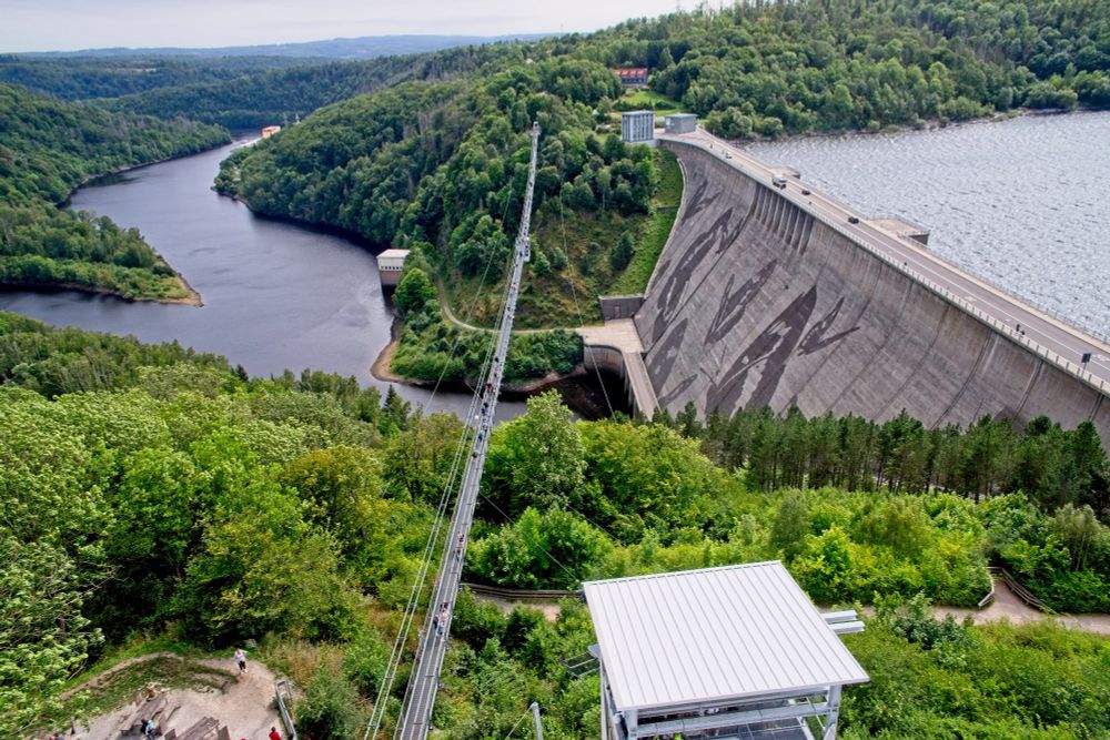 Die Rappbode-Talsperre, von einem Turm aus gesehen, neben der Staumauer, auf der Schmetterlingsmotive zu sehen sind, ist eine Hängebrücke und 2 Drahtseile. Auf der Brücke befinden sich Menschen.