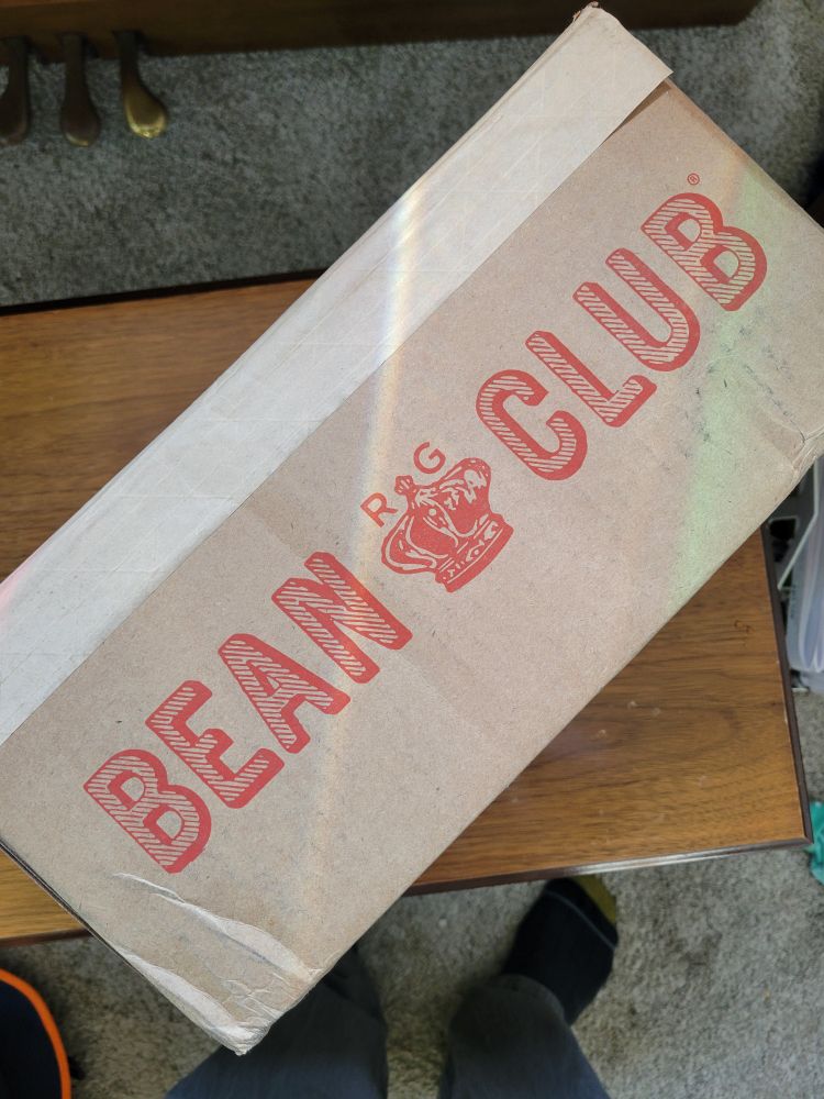 Photo of a rectangular cardboard box sitting on a piano bench; text and imagery indicating the "Rancho Gordo Bean Club" is visible