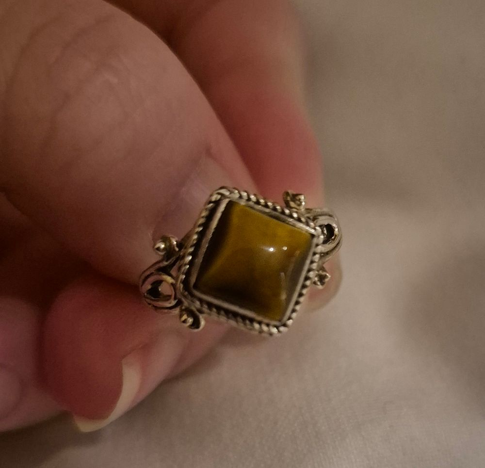 an intricate silver ring with a a square tiger eye in the middle