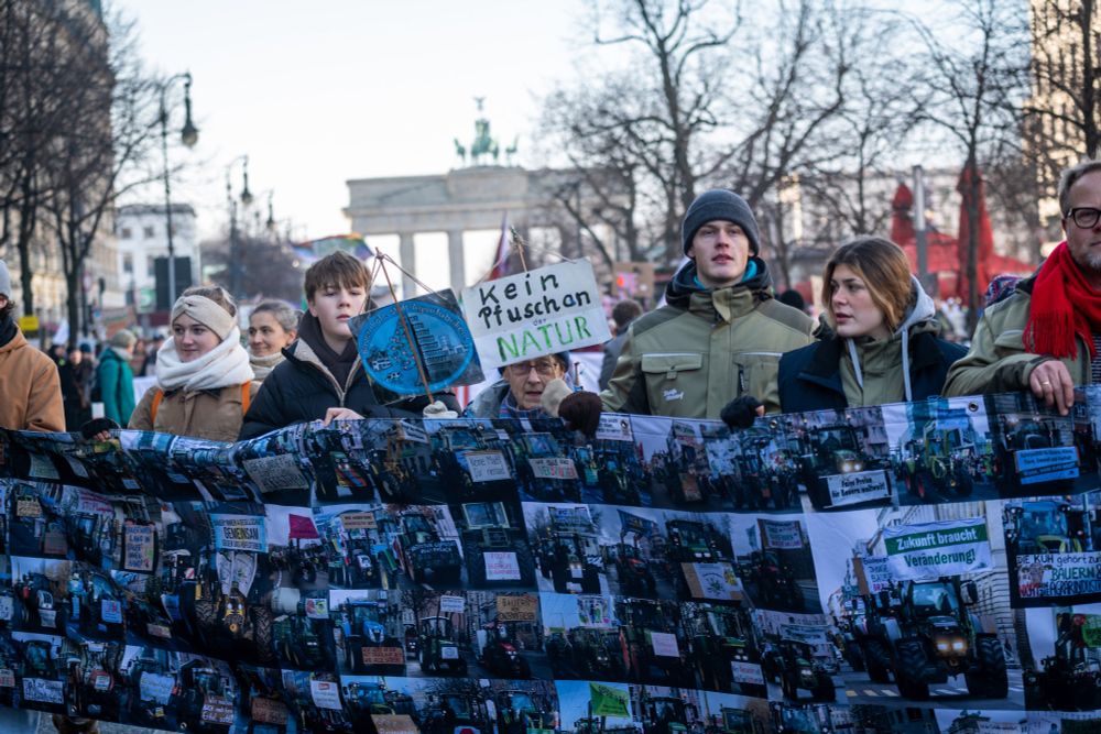 Bäuer*innen mit einem Banner, auf dem Trecker abgebildet sind, vor dem Brandenburger Tor.