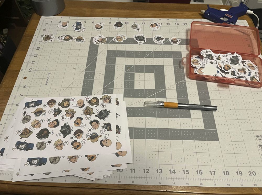 Photo - A table and cutting mat with a stack of uncut Fallout Companion stickers, along with a excato knife, and piles of trimmed and untrimmed stickers.