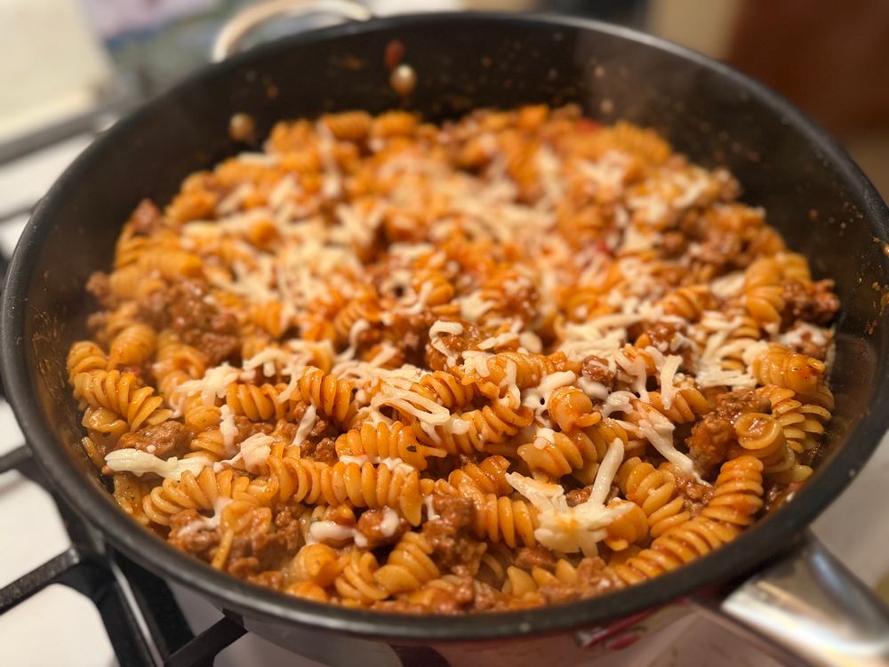 Rotini cooked in pasta sauce with ground beef, seasonings, and melted mozzarella in a big skillet on the stove 
