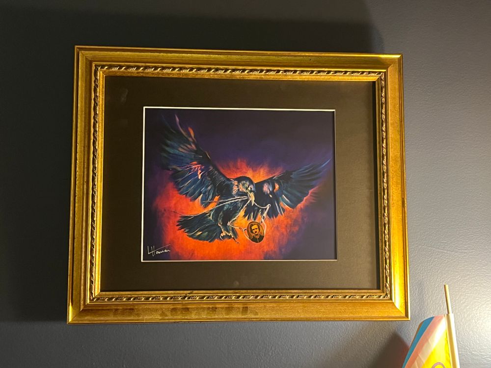 Painting of a crow with a locket of Edgar Allan Poe by Lynne Hansen in a gold frame 