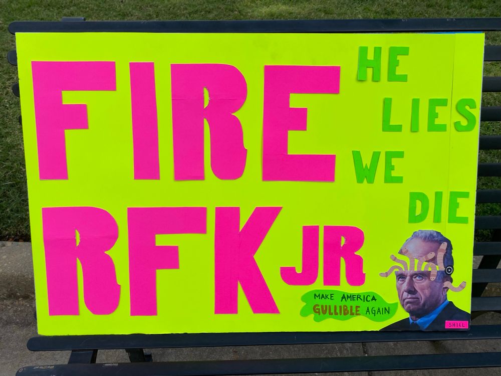 Protest sign stating “FIRE RFK Jr” and “He Lies, We Die” with a picture of a brainworm-infested RFK Jr saying “Make America Gullible Again.”