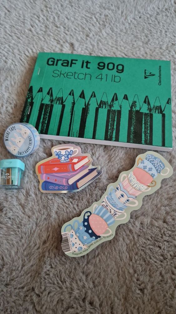 Piirustuslehtiä, washiteippi, pieni teroitin, tarra jossa kirjojen päällä teekuppi ja kirjanmerkki, joka on korkea kasa söpöjä teekuppeja.