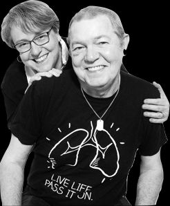 Black and white photo of Tony and Beth taken for an organ transplant promotion. Beth is standing behind Tony and he is wearing a dark t-shirt with a stylized drawing of lungs with the slogan, "live life, pass it on' on the front. You can see his medic-alert tag around his neck.