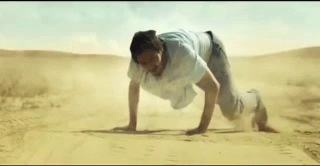 a man is crawling on his hands in the sand in the desert .