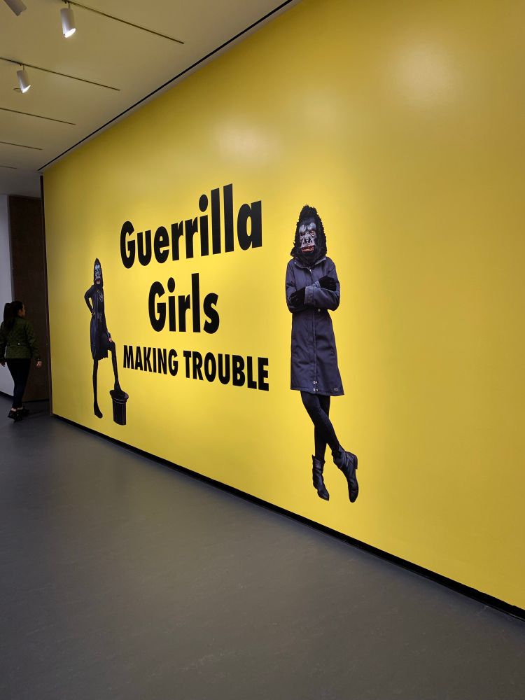Yellow wall with “Guerrilla Girls Making Trouble” written on it 