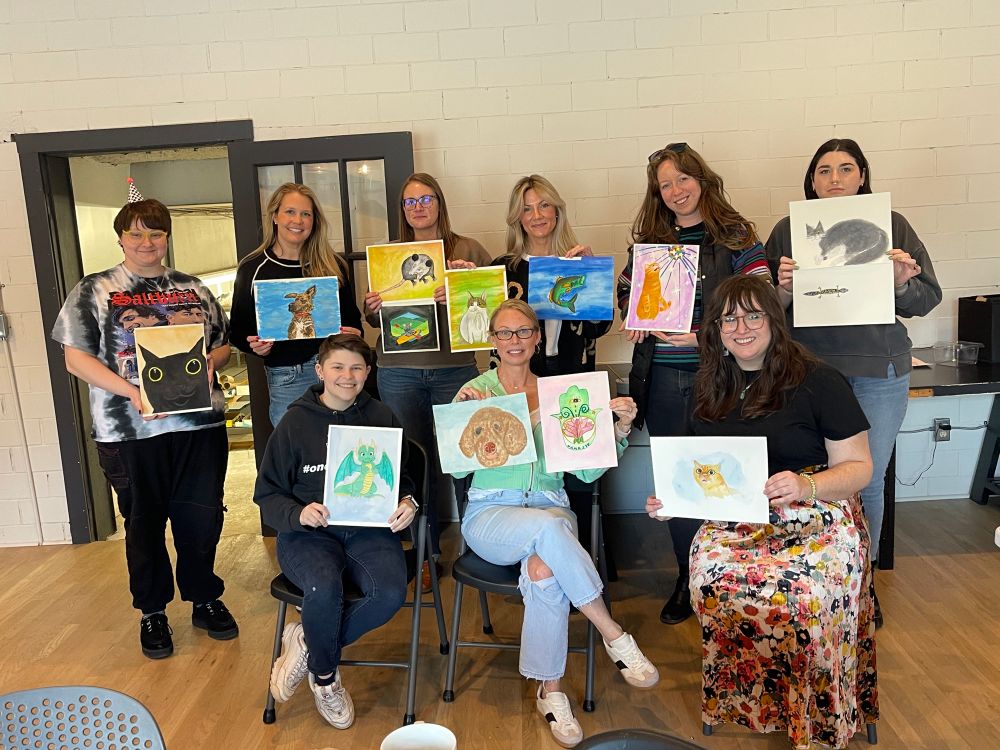A group photo of people holding up their paintings 